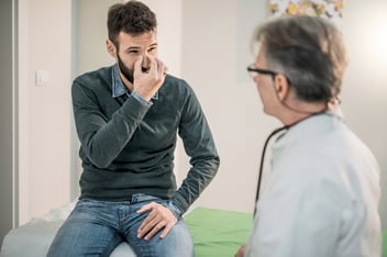 Man pinching the bridge of his nose during a facial plastic and reconstructive surgery consultation with a doctor in a medical office